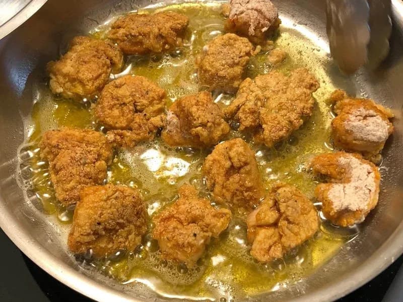 Breaded chicken and shrimp frying in golden oil in a stainless steel pan until light golden brown.