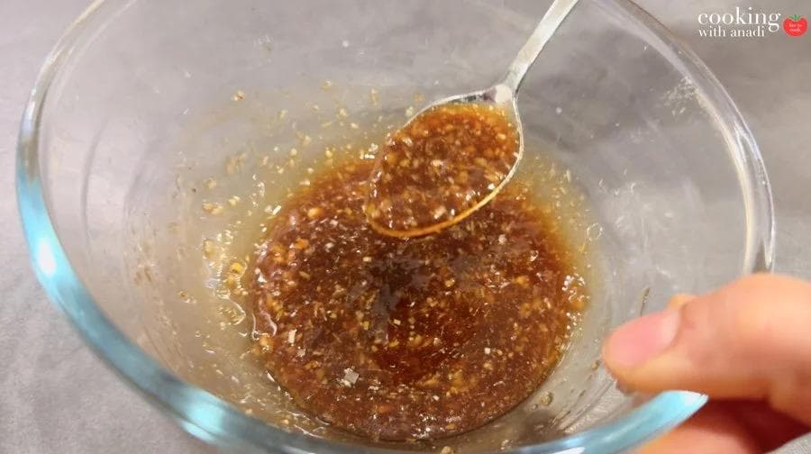 Dark brown marinade in a glass bowl, lifted with a spoon, showing a glossy, chunky sauce with visible garlic and spices.