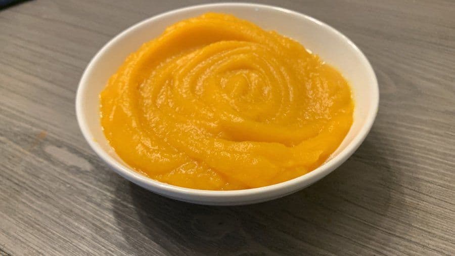 Smooth, thick pumpkin puree swirled in a white bowl on a gray wooden surface.