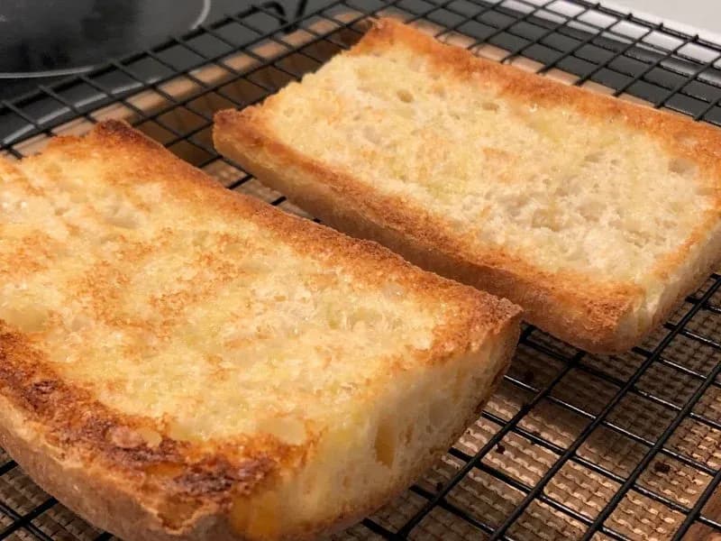 Two slices of toasted ciabatta bread with golden-brown, crispy edges cooling on a wire rack.