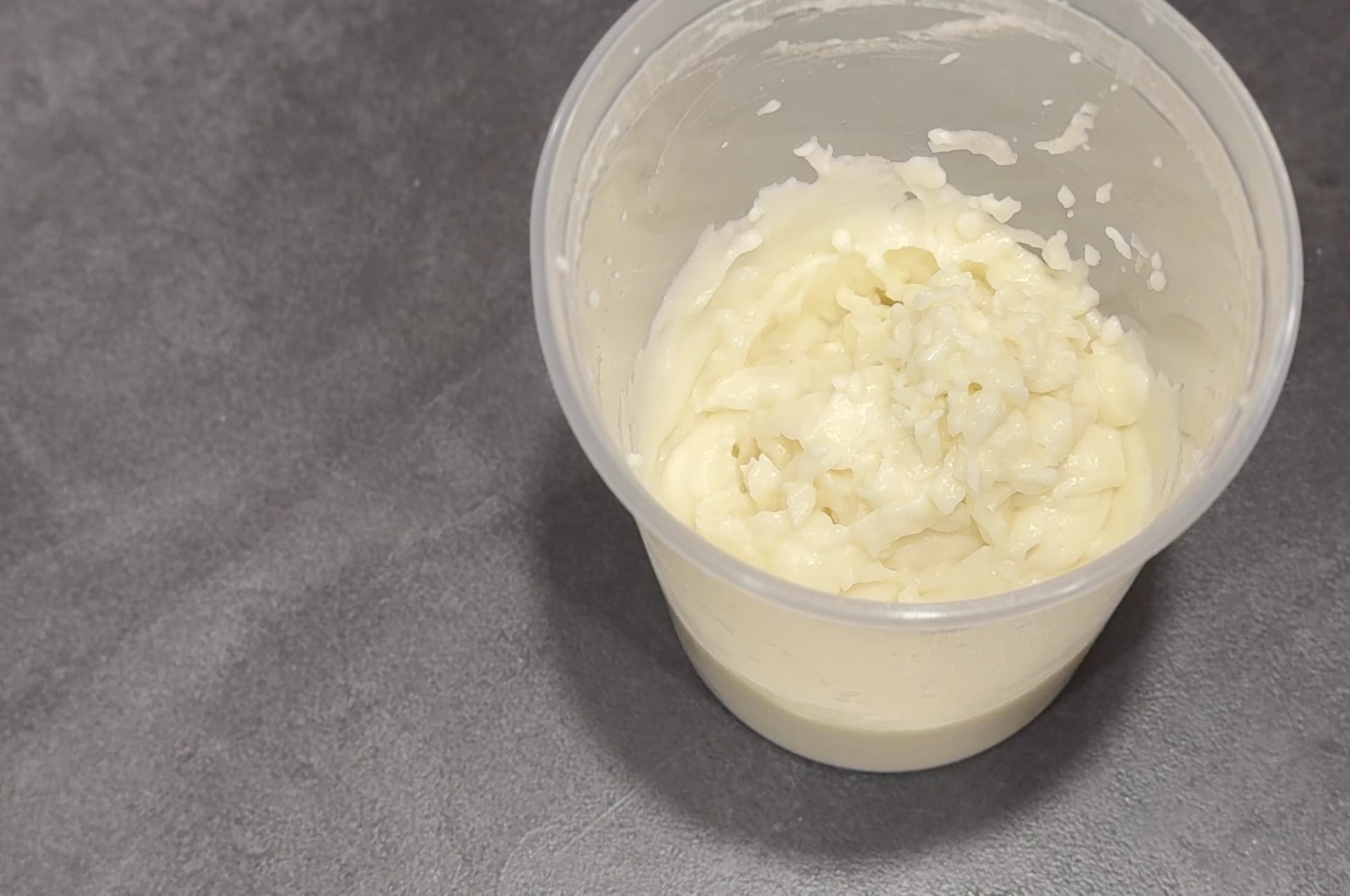 Creamy white toum emulsified in a clear container, showing the thick, fluffy texture after blending garlic with oil and lemon juice.