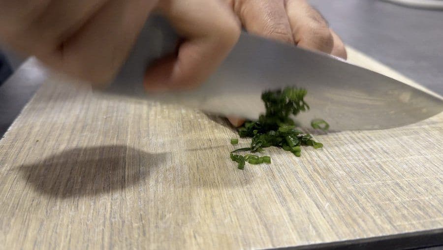 Chopping fresh green onions on a wooden cutting board with a chef's knife