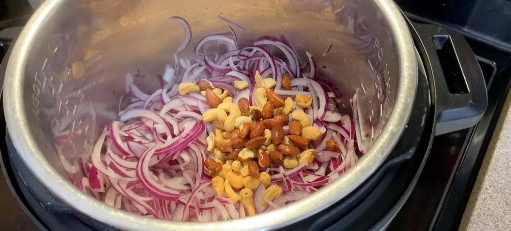 Sliced red onions, cashews, and almonds in an Instant Pot during sautéing stage of Chicken Changezi recipe.