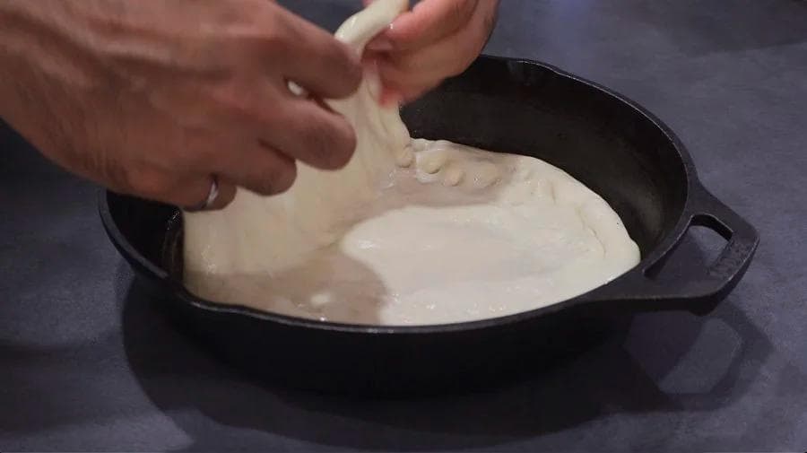 Stretching pizza dough in a black cast iron pan before topping and baking.