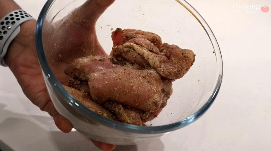 Chicken thighs coated in spice rub of salt, oregano, cumin, and pepper in a glass bowl.