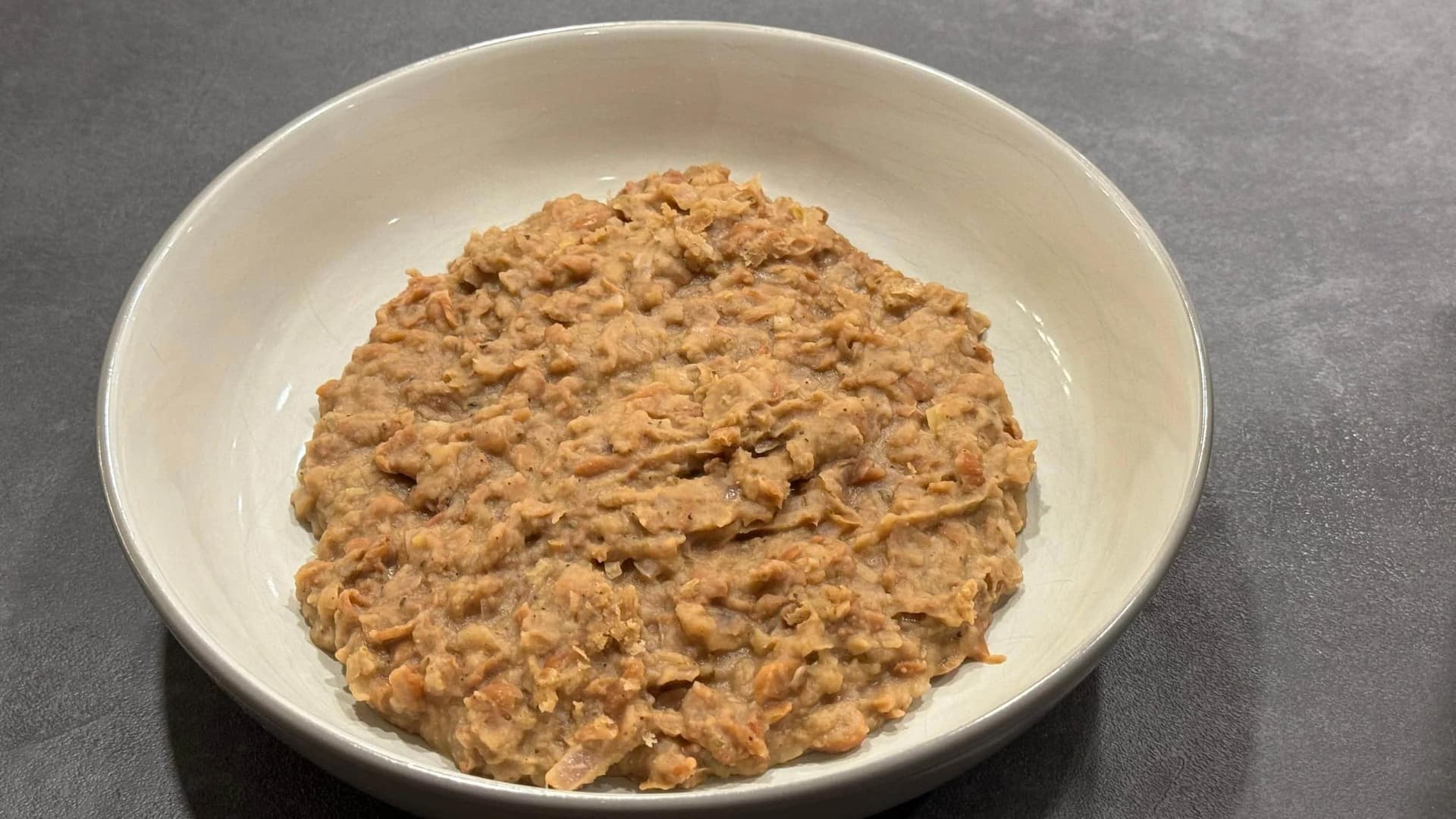 Homemade refried beans with a thick, chunky texture in a white bowl, seasoned with cumin and oregano.