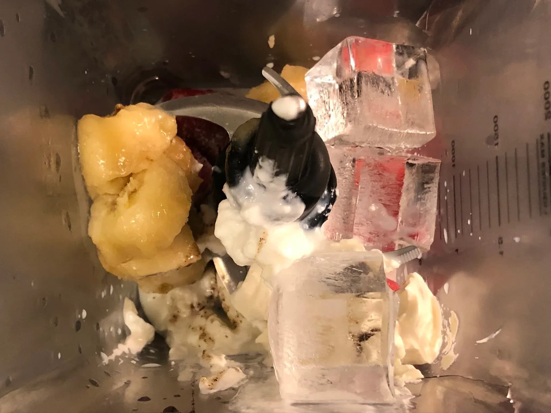 Blender pitcher filled with ice cubes, cream cheese, and other smoothie ingredients ready to blend.