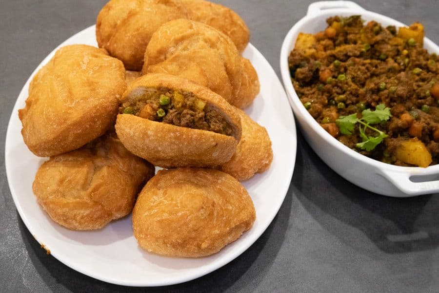 Crispy golden vetkoek with curry beef filling served alongside spiced mince curry in a white bowl.