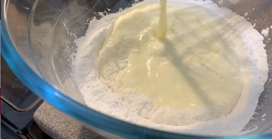 Wet pancake batter being poured into a bowl of dry ingredients with a whisk, mid-mixing stage.