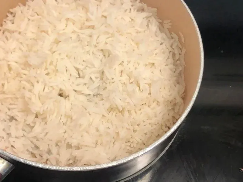 Cooked white rice in a stainless steel pan, ready to be added to the pan with sautéed onions and spices.