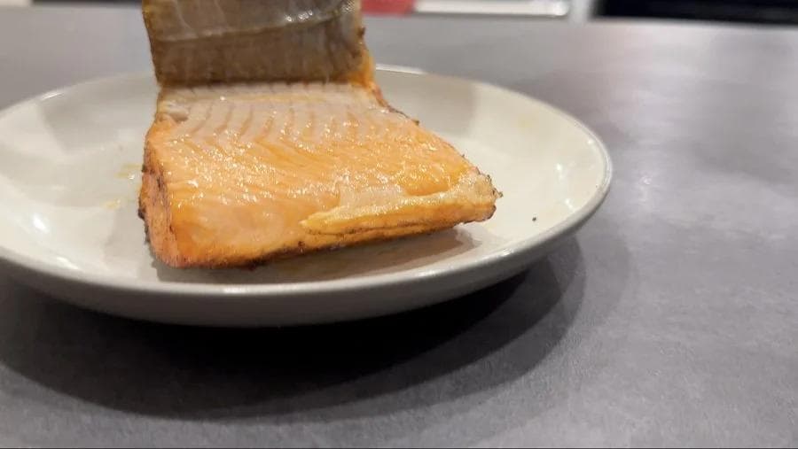 Cooked salmon fillet with crispy skin on a white plate, ready to serve.