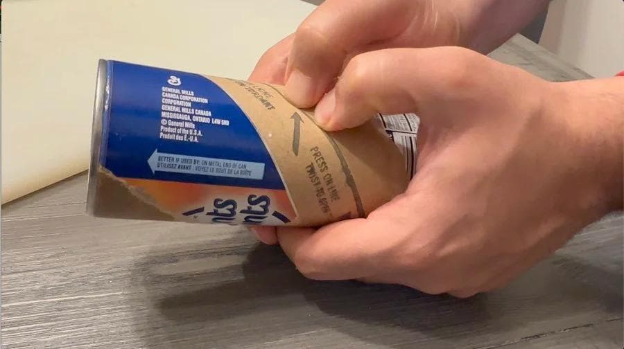 Hand holding a can of crescent roll dough over a wooden surface.