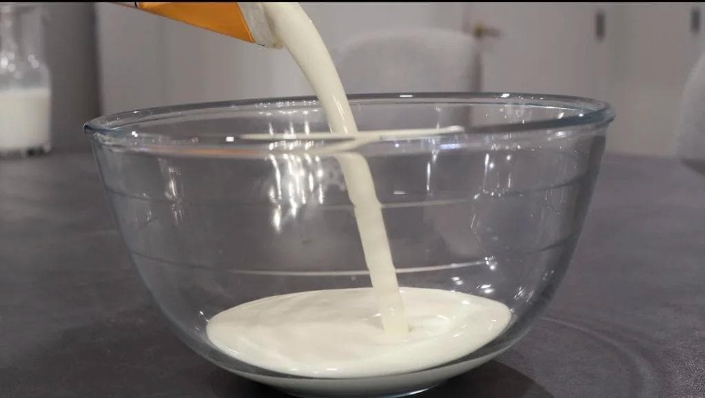 Heavy cream being poured into a glass bowl with a whisk, creating soft peaks for whipped cream.