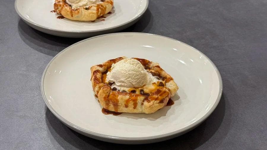 Two mini puff pastry apple pies topped with vanilla ice cream on white plates.