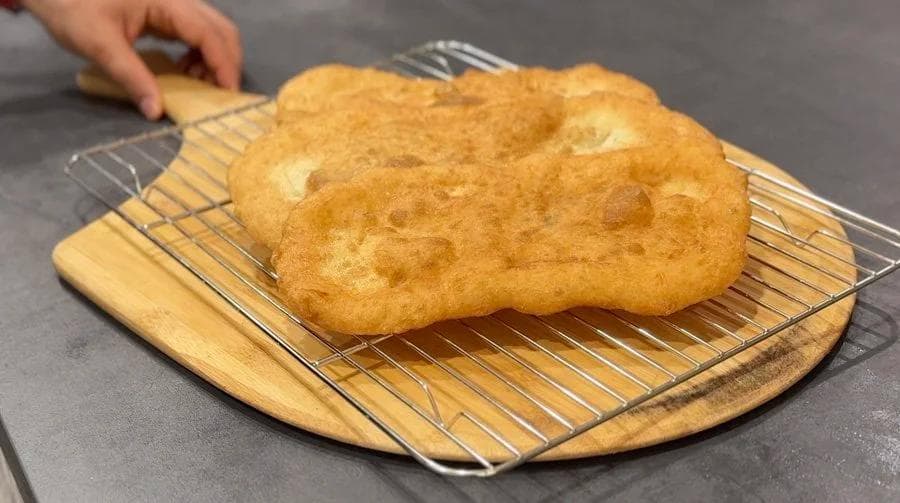 Golden-brown fried beavertail pastry cooling on a wooden board with wire rack.