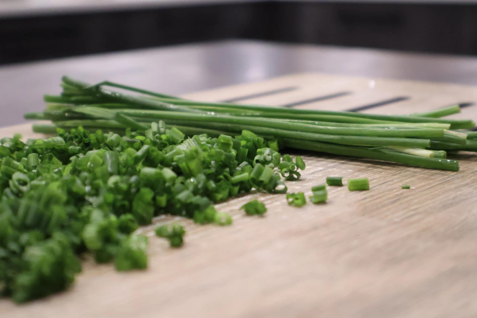 Fresh green onions and chives chopped on a wooden cutting board for herb butter preparation.
