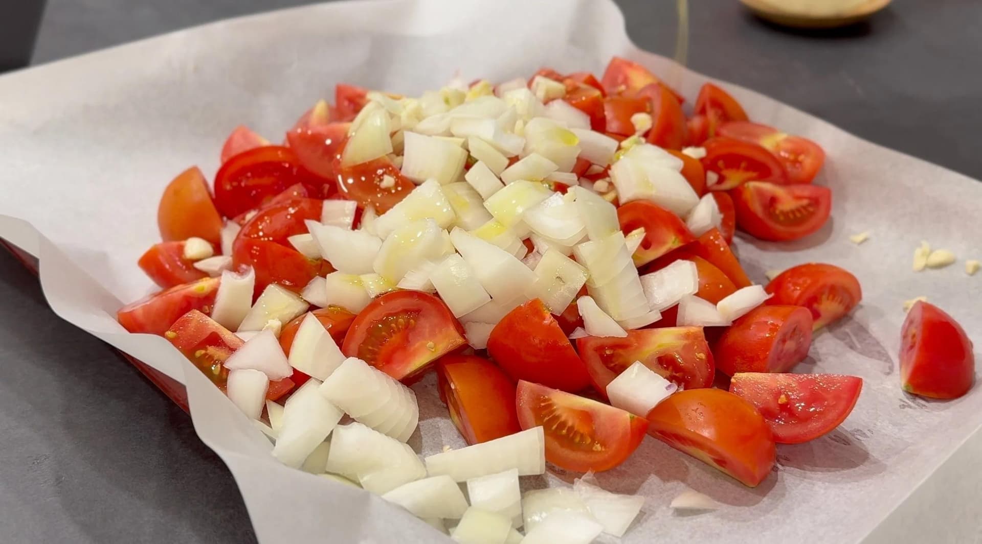 Diced onions and tomato quarters on parchment paper, ready for roasting in the oven.