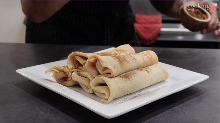 Rolled pumpkin crepes dusted with cinnamon on a white square plate, ready to serve.