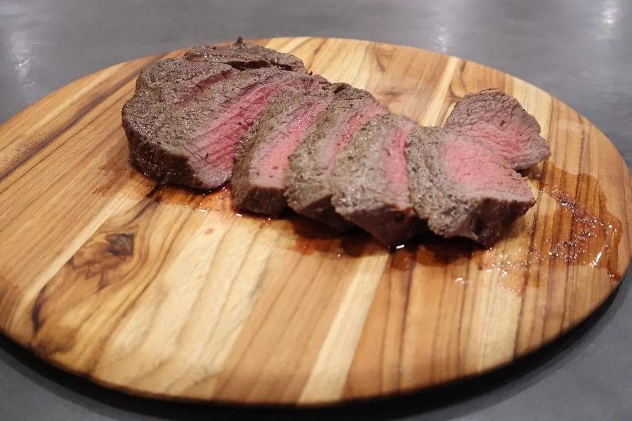 Sliced air fryer sirloin steak with pink medium-rare center on a wooden cutting board.