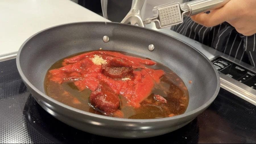 Red Korean sauce simmering in a gray pan with cooked tofu pieces, thickened and ready to be removed from heat.