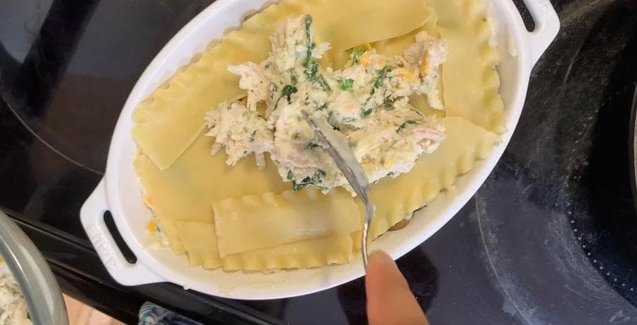 Unbaked chicken lasagna in white baking dish with layers of pasta sheets, creamy filling, and cheese topping ready for baking.