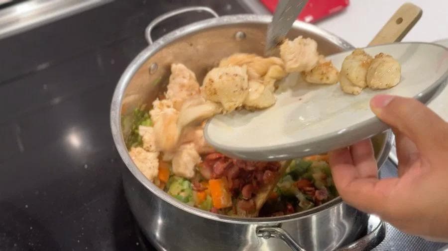 Chicken stew with dumplings being added to pot containing browned chicken, bacon, and vegetables.