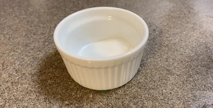 White cinnamon sugar mixture in a small white ceramic bowl on a gray countertop.