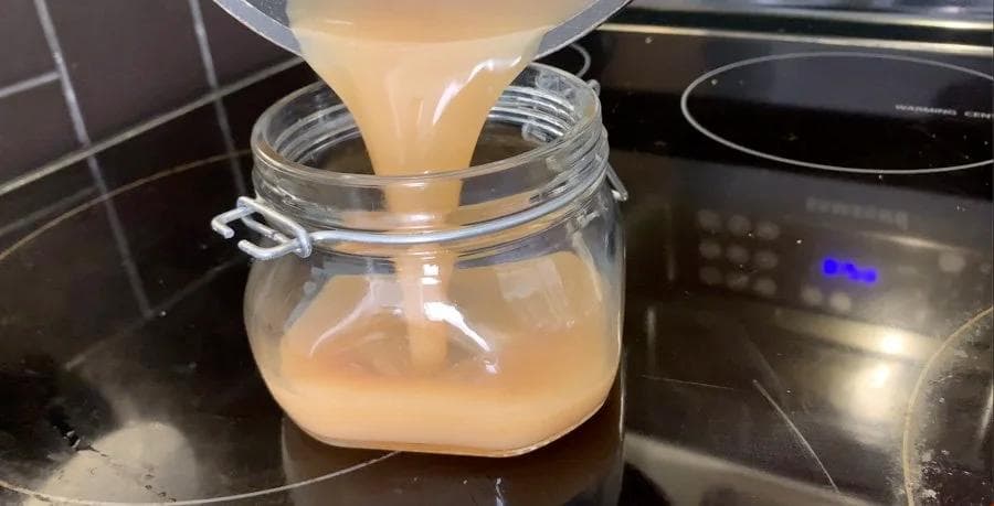 Homemade caramel sauce being poured into a glass jar to cool, showing its rich amber color.