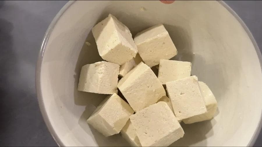 Cubed tofu pieces arranged in a white bowl, showing proper portioning and moisture removal for air frying.