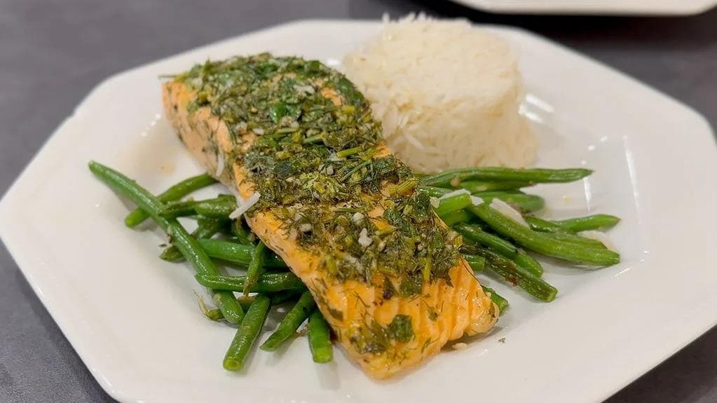 Herb-crusted baked salmon fillet with green beans and mashed potatoes on a white plate