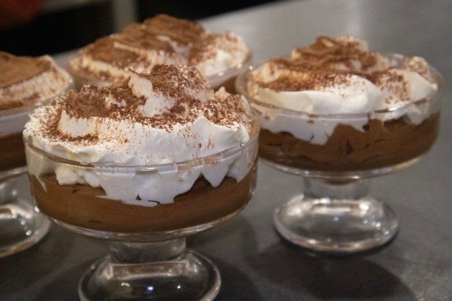 Three chocolate mousse desserts in glass cups topped with whipped cream and cocoa powder.