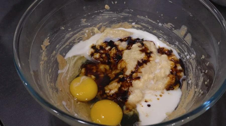 Wet ingredients for gingerbread banana bread including mashed bananas, eggs, milk, and molasses in a mixing bowl.