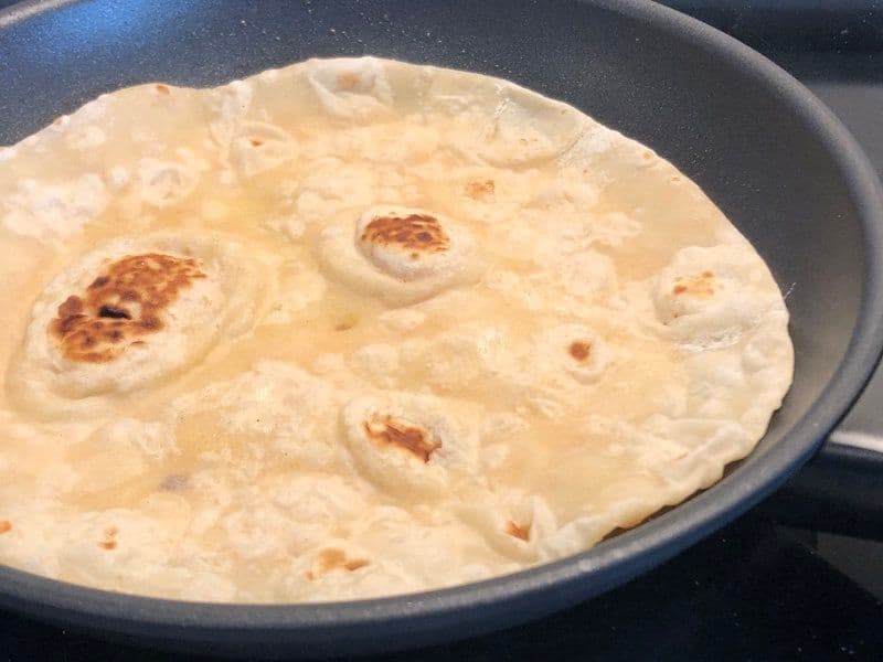 Cooked egg coating the underside of a paratha in a dark skillet, with brown spots visible on the egg surface.