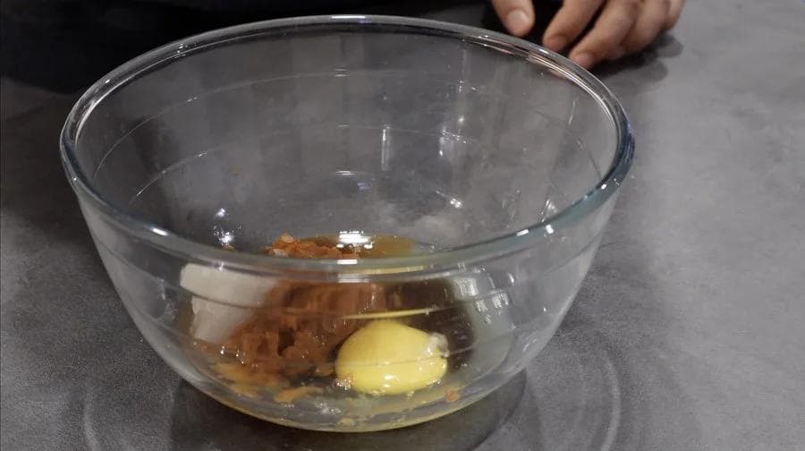 Wet ingredients mixed in a glass bowl: egg, maple syrup, pumpkin puree, and coconut oil combined together.