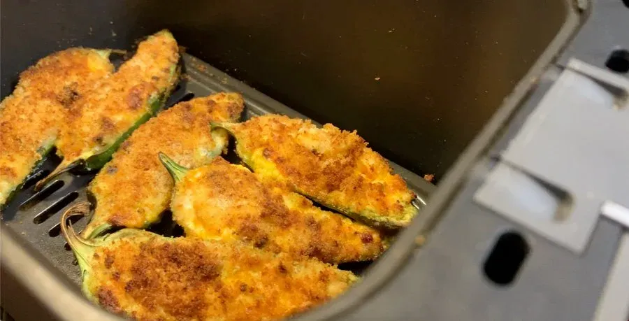 Golden-brown breaded jalapeño poppers in an air fryer basket, garnished with fresh rosemary sprigs.