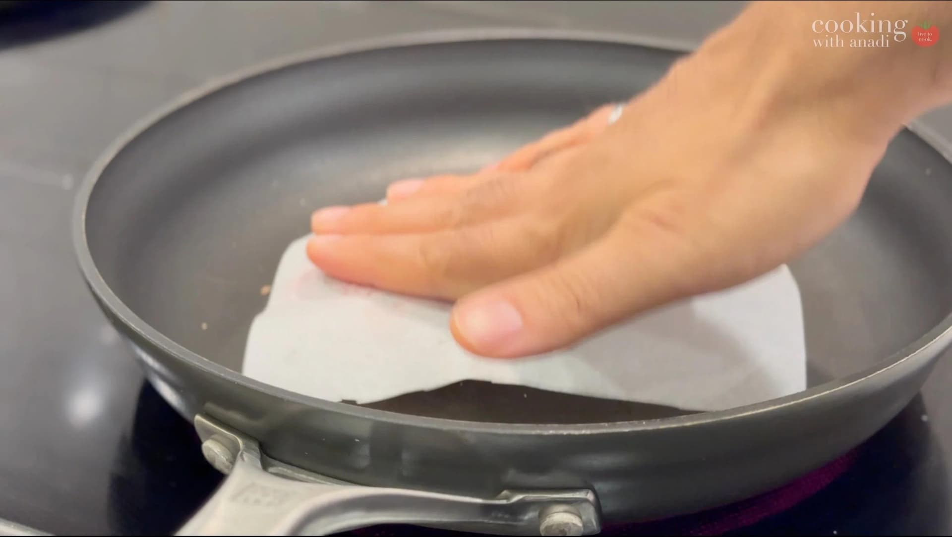 Hand pressing a white patty with parchment paper in a nonstick skillet on the stove.