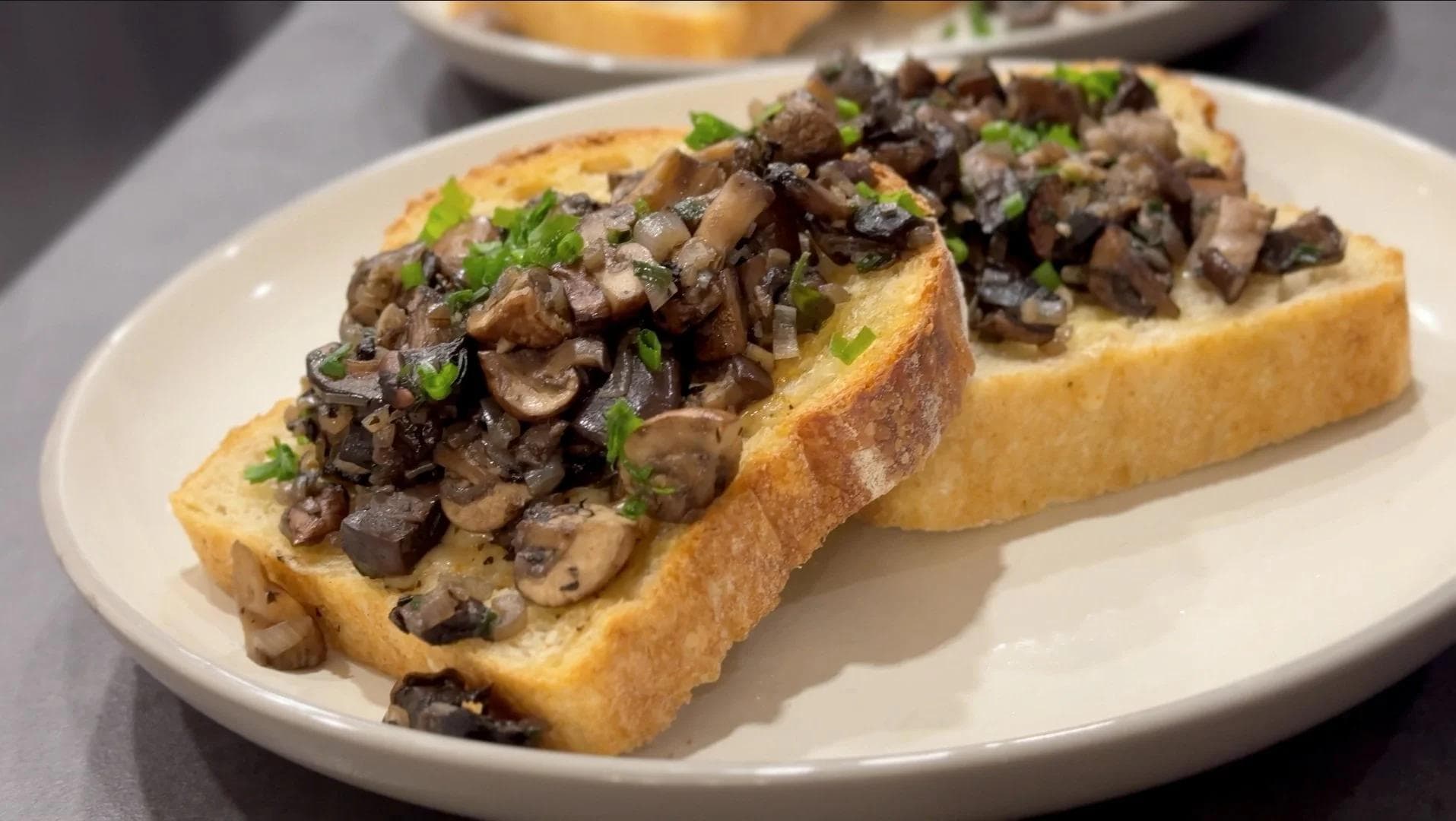 Mixed mushrooms sautéed with caramelized onions and herbs served on toasted bread slices on a white plate.
