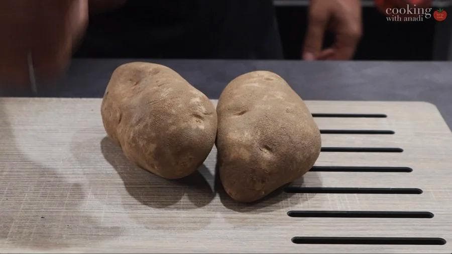 Two whole potatoes on a wooden cutting board with measurement lines, ready to be prepared for air frying.