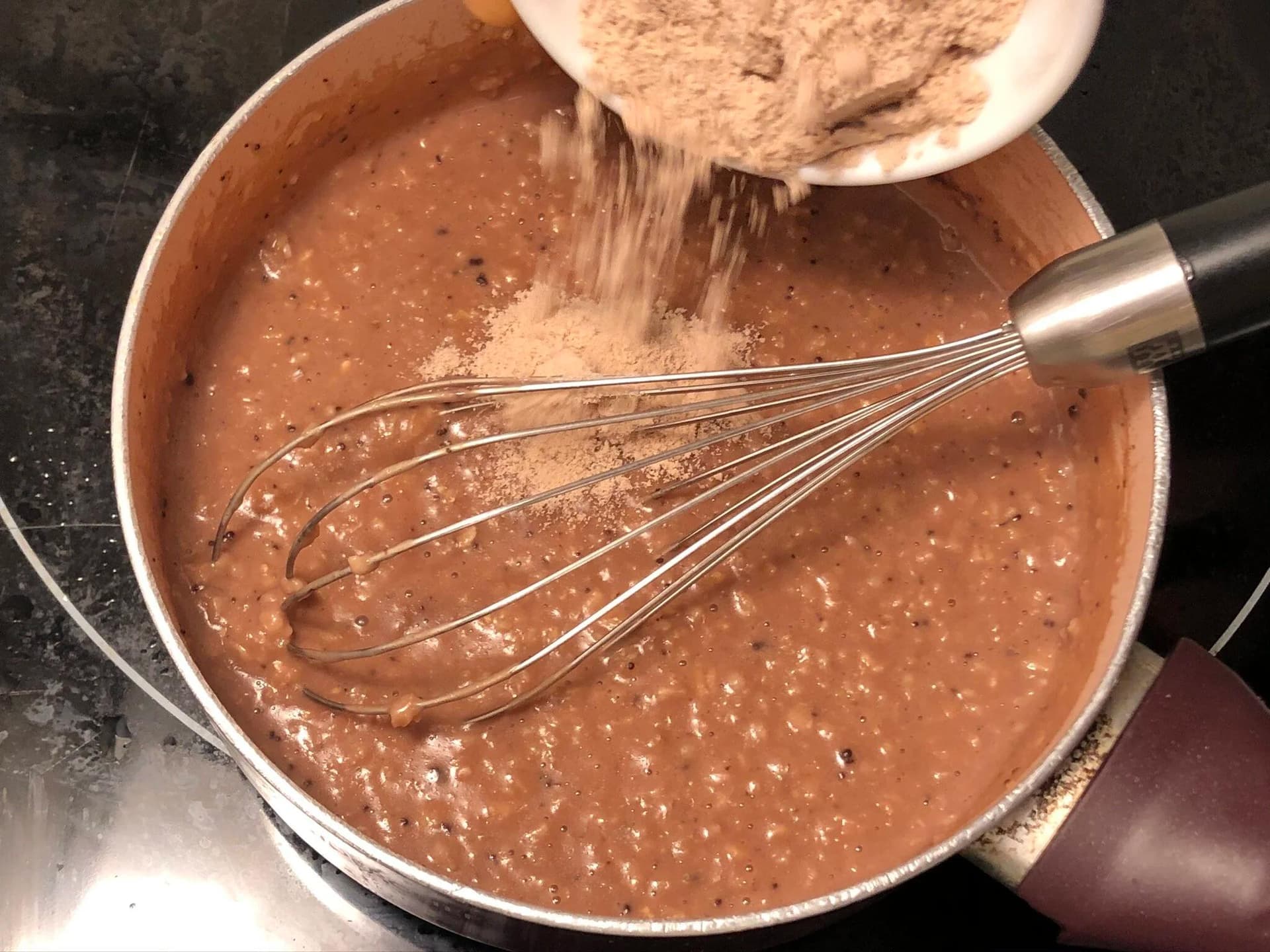 Whisking chocolate protein powder into oatmeal in a pot with a whisk to remove lumps.