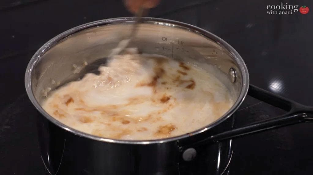 Steel-cut oats simmering in a black pot with milk and molasses swirled in, showing a creamy beige mixture.