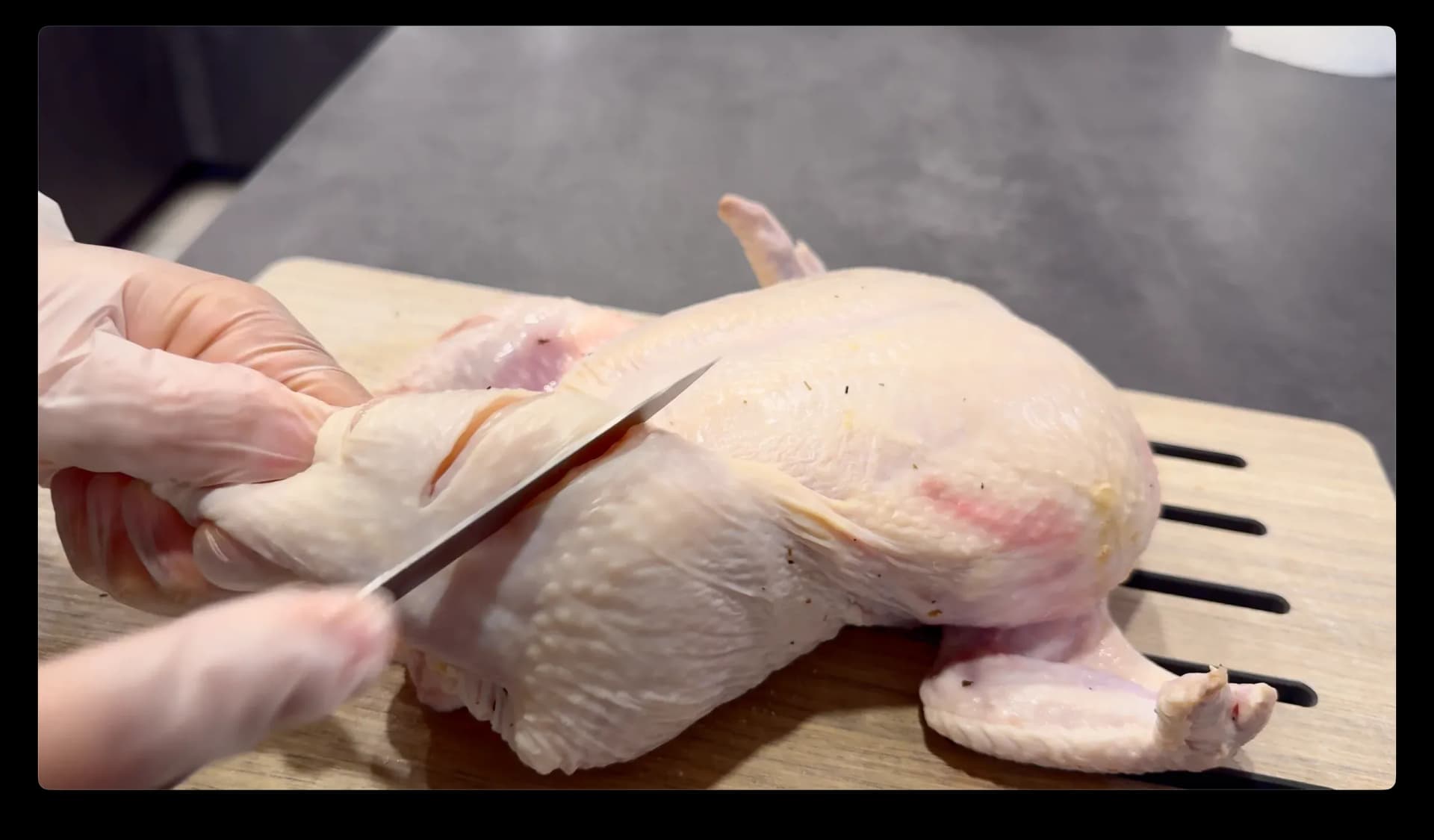 Chef making slits into raw chicken leg with a sharp knife on a cutting board