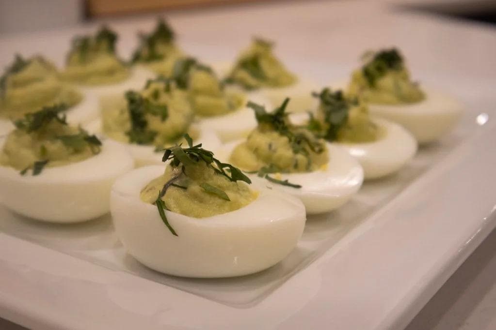 Deviled eggs with avocado-herb filling garnished with fresh tarragon on white plate