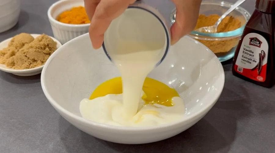 Pouring cream into a bowl with egg yolks and pumpkin puree for tempering in pumpkin rice pudding recipe.