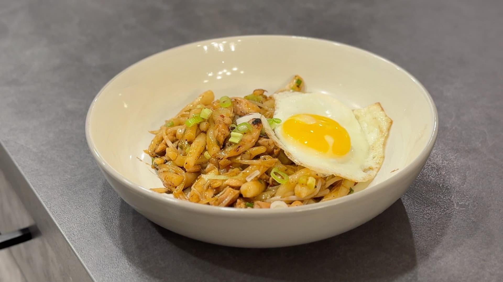 Lort Cha noodles in a white bowl topped with a fried egg and garnished with green onions.