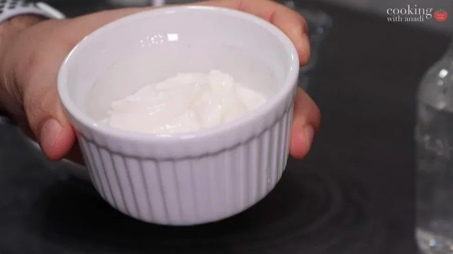 Yogurt in a white bowl held in hands for bhature dough preparation