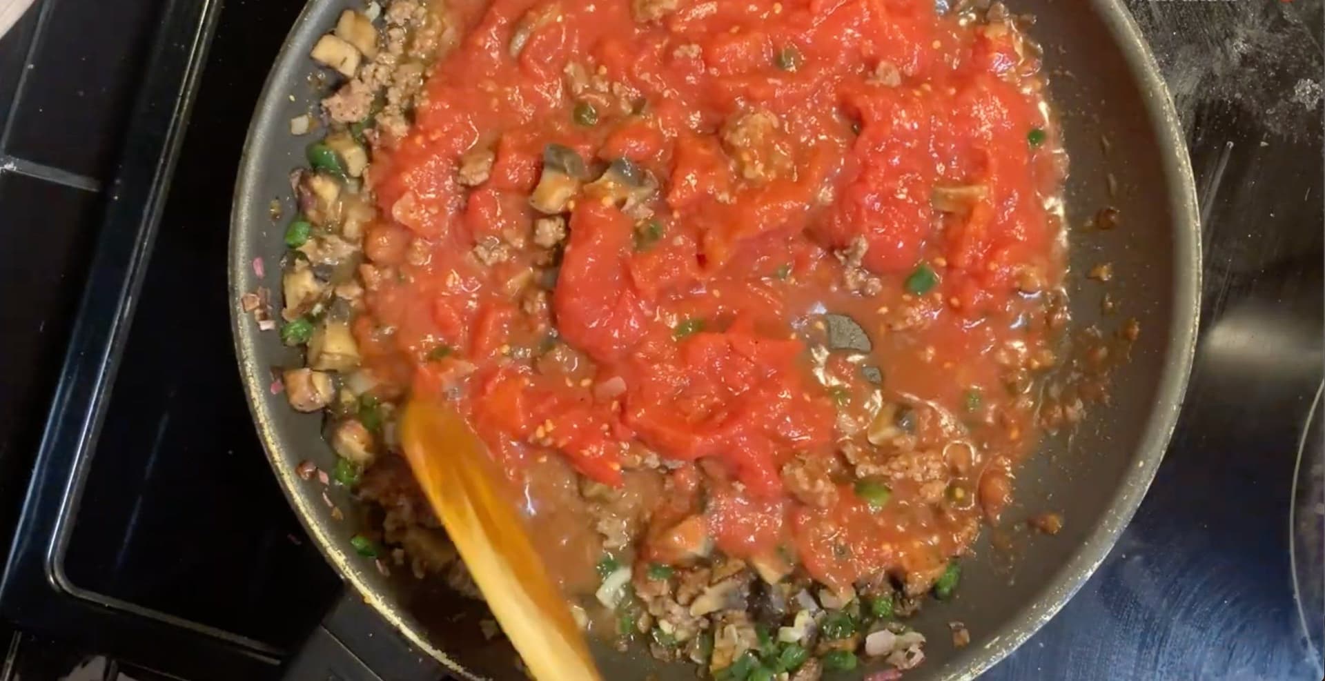 Ground meat sauce with crushed tomatoes and herbs simmering in a pan on the stovetop.