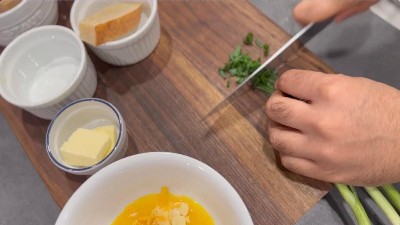 Egg yolks mixed with chopped green onions, cheese, and seasonings in a white bowl on a wooden cutting board.