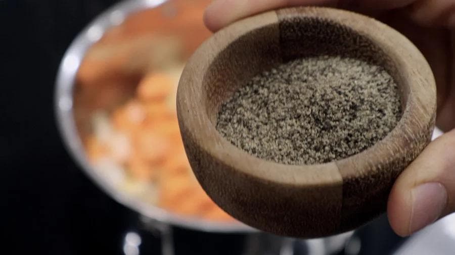 Ground black pepper in a wooden mortar being added to carrot soup ingredients.