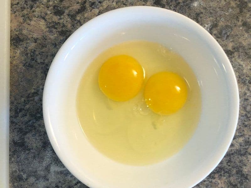 Two whisked eggs in a white bowl with ghee, ready to be poured into the pan.