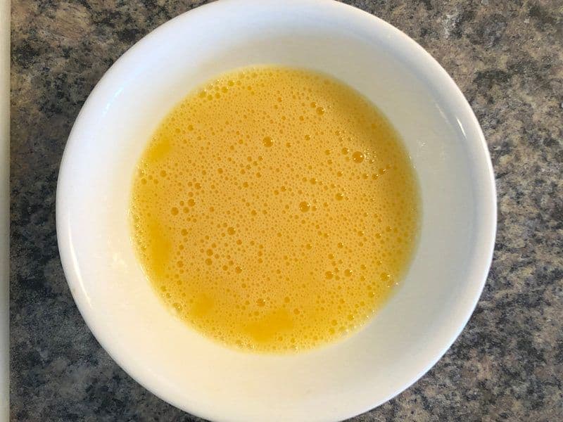 Whisked eggs with bubbles in a white bowl, ready to be cooked for the chicken kathi roll.